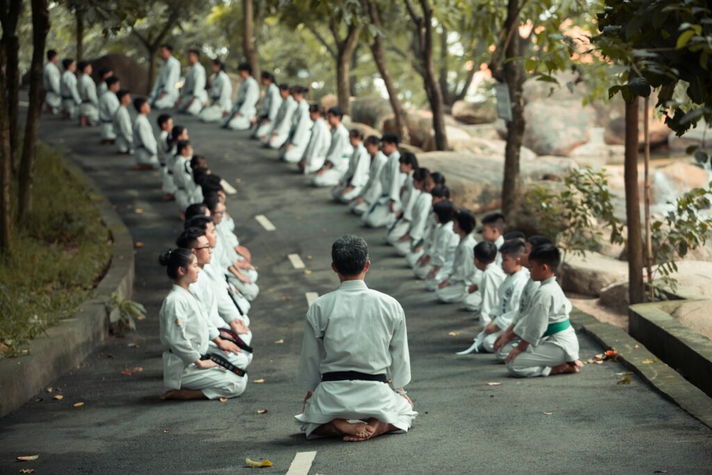 Group of people in white uniforms meditating in a forest setting.